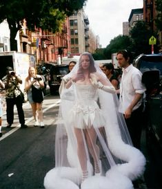 a woman in a white wedding dress standing on the street with her veil over her head