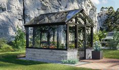 a small house with plants in it near a rock wall