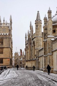 people are walking down the street in front of old buildings with snow on their roofs