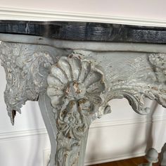 an old white table with ornate carvings on it's sides and wood flooring