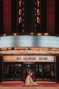 a bride and groom pose in front of the elginton grand theater for their wedding photo