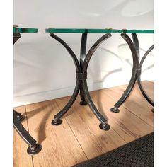 a glass top table with metal legs on wooden flooring next to a white wall