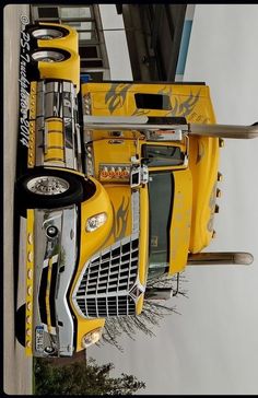 a yellow semi truck parked next to a tall building