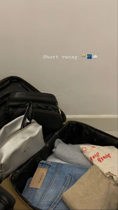 an open suitcase sitting on the floor next to a wall with short vacay written on it