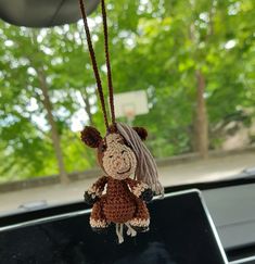 a crocheted stuffed animal hanging from a car's dash board with trees in the background