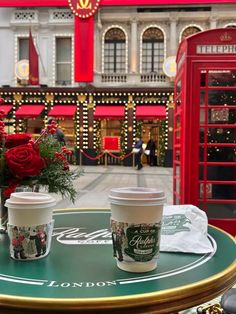 two cups of coffee sitting on top of a table in front of a red phone booth