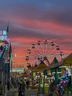 an amusement park at dusk with ferris wheel and fairground in the background as people walk around