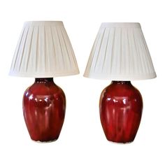 two red vases with white lamps on top of each one, sitting side by side