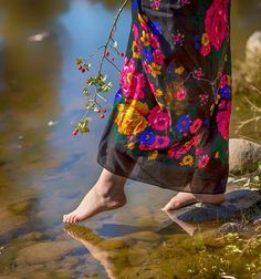 a woman standing in the water with her feet up and holding onto a branch that has flowers on it