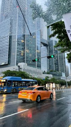 a city street filled with traffic next to tall buildings and green traffic lights on a rainy day