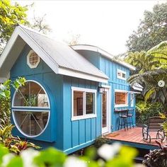 a small blue house in the middle of some trees and bushes, with a deck leading to it