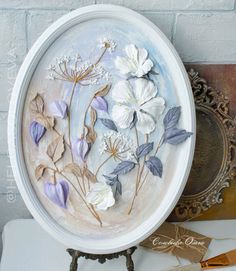 a white plate with purple and white flowers on it next to an ornate frame,