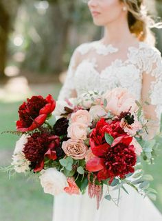 a bride holding a bouquet of red and pink flowers on her wedding day in the park