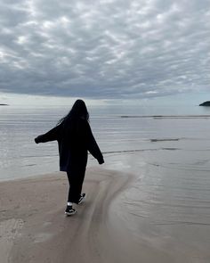 a woman walking on the beach with her arms spread out in front of the ocean