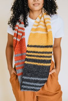 a woman wearing an orange, yellow and black striped crochet scarf with her hands in her pockets