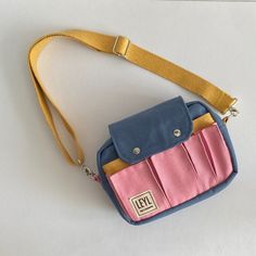 a small blue and pink purse sitting on top of a white table next to a yellow strap