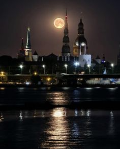 the full moon is seen in the sky over some buildings on the river at night