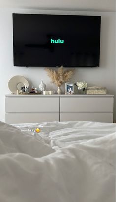 a flat screen tv mounted on the wall above a bed with white sheets and pillows