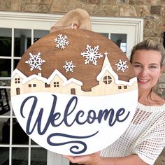 a woman holding up a welcome sign in front of a house with snowflakes on it