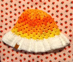 a crocheted hat on top of a pink and orange fabric with strawberries in the background