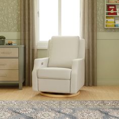 a white rocking chair sitting in front of a window next to a rug and dresser