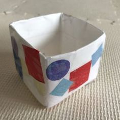 a paper bowl sitting on top of a white table covered in blue, red and pink shapes