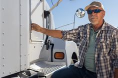 a man in plaid shirt and hat sitting on the side of a white semi truck