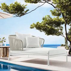 a white chaise lounge chair sitting next to a pool with an umbrella over it