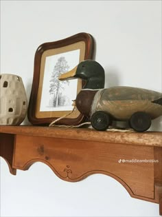 a wooden duck sitting on top of a shelf next to a framed photo and other items