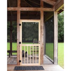 a wooden porch with an open door and screen on the front entrance to a large grassy area