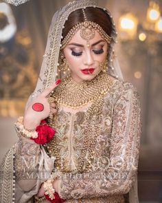 a woman in a bridal outfit with red flowers on her head and hands near her face