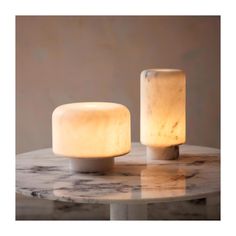 two white candles sitting on top of a marble table next to each other and one is turned off