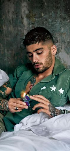 a man sitting in bed holding a lit candle and looking at his cell phone with one hand