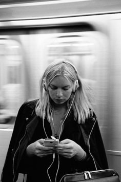 a woman with headphones is looking at her cell phone while riding the subway train