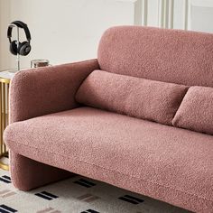 a pink couch sitting on top of a rug next to a gold table with headphones