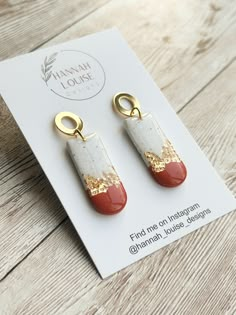 two red and white earrings with gold accents on top of a wooden table next to a card