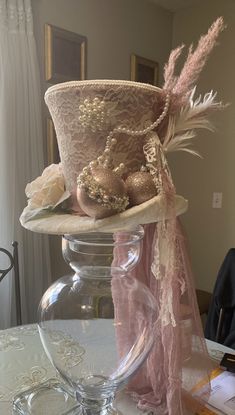 a hat is sitting on top of a glass vase with pink flowers and feathers in it