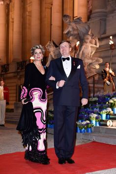 a man and woman standing on a red carpet in front of a building with statues