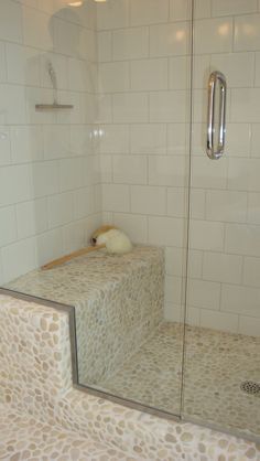 a walk in shower sitting next to a white tiled wall and floor with a glass door