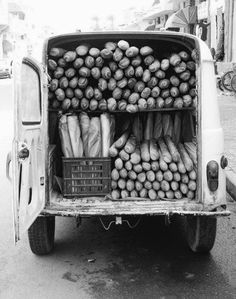 an old truck is loaded with potatoes and carrots on the street in black and white