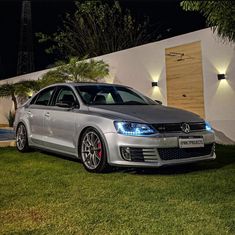 a silver car parked in front of a white house at night with its lights on