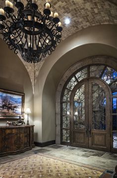 a chandelier hangs from the ceiling in front of an arched doorway with glass panels