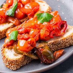 two pieces of bread with tomatoes and basil on top, sitting on a gray plate