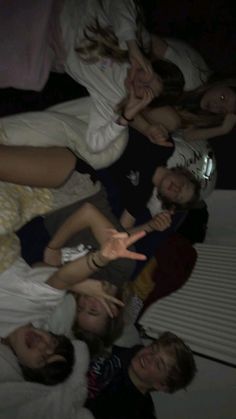 a group of young people laying on top of a bed in a room with white sheets