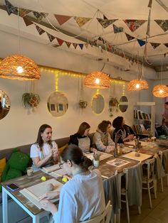 a group of people sitting around a table in a room with lights hanging from the ceiling