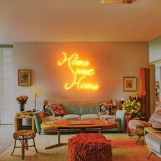 a living room filled with furniture and a neon sign on the wall above it that says home sweet home