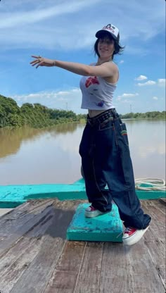 a woman standing on top of a wooden dock next to a body of water with trees in the background