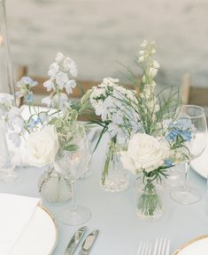 the table is set with white and blue flowers in vases, silverware, and plates