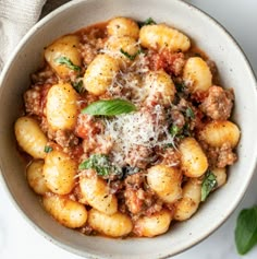 a white bowl filled with pasta and sauce on top of a marble table next to a napkin