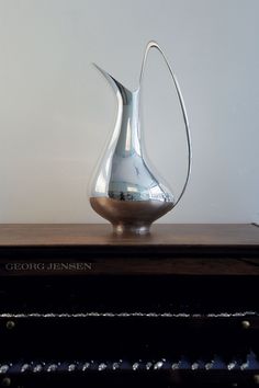 a silver vase sitting on top of a wooden table next to a keyboard and piano